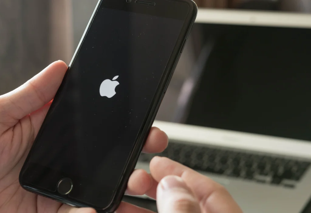 Mãos segurando um iPhone que está na tela da maçã ou seja reiniciando num loop infinito.